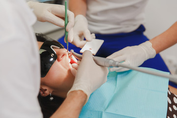A male dentist with a female assistant helps to treat the teeth of a woman patient in a clinic in the office, close-up