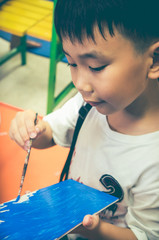 Happy asian boy painting blue color on artwork with paintbrush.