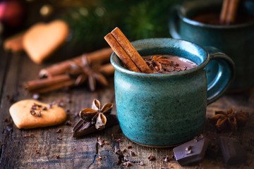 Obraz na płótnie Canvas Hot chocolate with a cinnamon stick, anise star and grated chocolate topping in festive Christmas setting on dark rustic wooden background