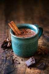 Tasse de chocolat chaud avec un bâton de cannelle, anis étoilé et chocolat noir râpé comme garniture sur fond de bois rustique foncé
