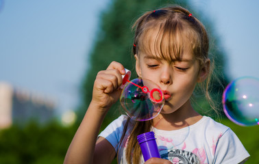 Close-up girl of six-years blowing bubble in a public park.