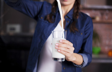 Female hands pour milk into a glass on the kitchen background