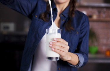 Female hands hold a full glass of fresh milk on the kitchen background