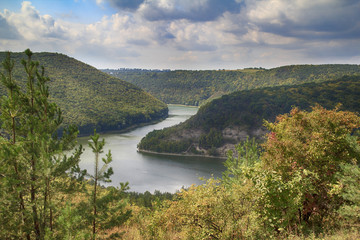 Autumn landscape with rivers bend between green hills with spruces and trees at foreground