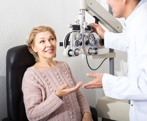 Mature optician examinating eyesight with aid of slit lamp