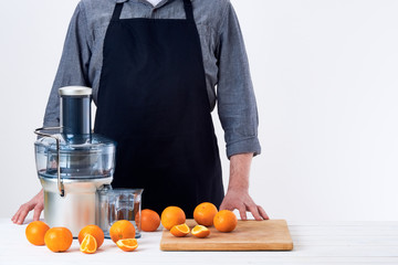 Anonymous man wearing an apron, preparing freshly made orange juice, using modern electric juicer,...