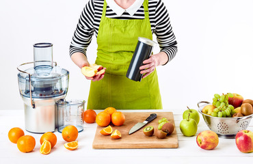 Anonymous woman wearing an apron, preparing fresh fruit juice using modern electric juicer, healthy...