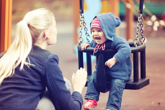 Mother With Her Child Having Fun On Playground Swing On Autumn Day