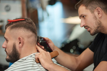 Young professional male barber concentrating while giving his customer a haircut. 