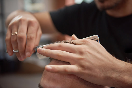 Cropped close up of a professional barber using scissors and comb while giving a haircut to his client. 