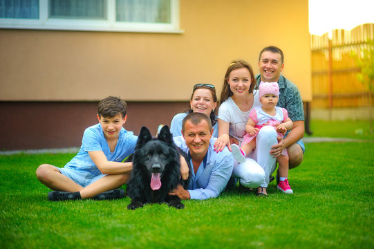 Happy Friendly Family Together With A Big Black Dog Lies On The Lawn Near His House