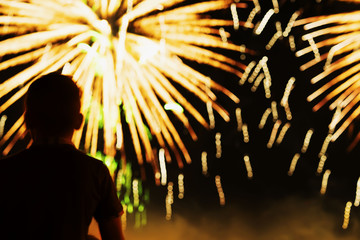 Unrecognizable silhouette of a boy with his back to us, who watches the show Fireworks. Festive...