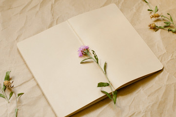 Top view of notebook empty page, Notebook with dry flowers beside on old crumpled brown paper background. Free text space. Copy space.