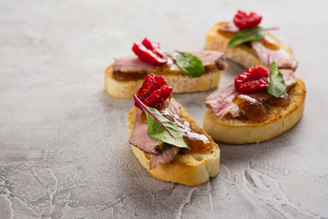 Bruschetta sandwiches with duck meat, fig sauce and berries on stone table. Space for text