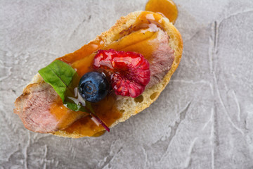 Bruschetta sandwiches with duck meat, fig sauce and berries on stone table. Space for text
