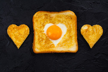 Heart shaped fried egg baked in a toast. Tasty breakfast for Valentines day on black background. Space for text