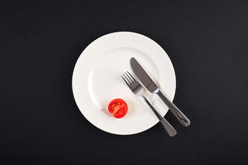 Top view of white dish with tomato on background of black table
