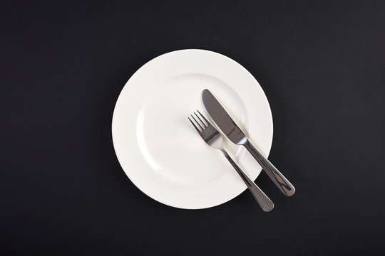 Top view of white dish with fork and spoon on background of black table