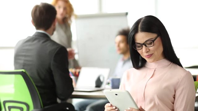 Meeting room in the office, brunette woman on front view holding tablet in hands. Corporate meeting, manager looking at tablet.