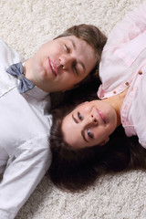 Happy woman and young handsome man in bow tie lie on carpet, top view