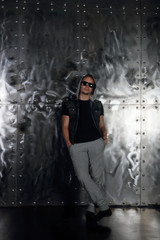 Young man in sunglasses poses near metal wall in modern studio