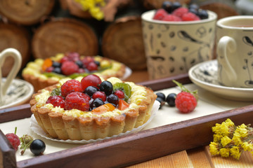 Small tart with raspberry, redcurrant, blackcurrant, peach, kiwi, cream on wooden tray - sweet dessert