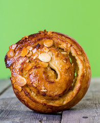 närbild på en bulle med mandelflarn mot grön bakgrund balanserar på sin ena sida på ett rustikt trä bord