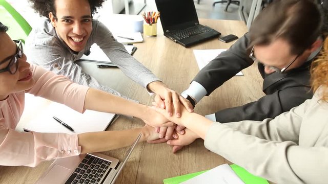 Close up view of business team sitting at the table in the office, folding hands. Work is done, happy coworkers holding hands together.