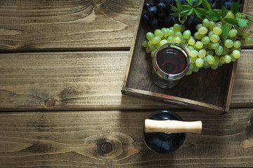 Open bottle of wine with a glass, corkscrew and ripe grape in tray on a wooden background. Copy space and top view.