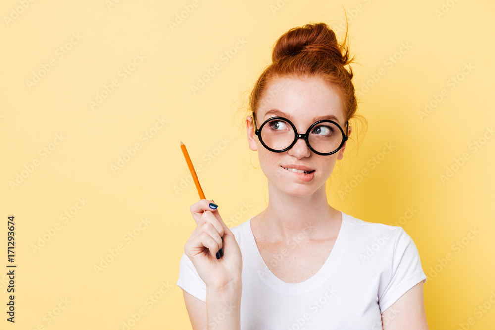 Wall mural mystery ginger woman in eyeglasses bites her lip with pencil