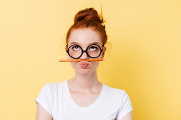 Funny ginger woman in eyeglasses playing with pencil