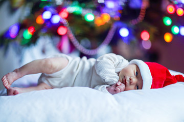 One week old newborn baby in Santa hat near Christmas tree