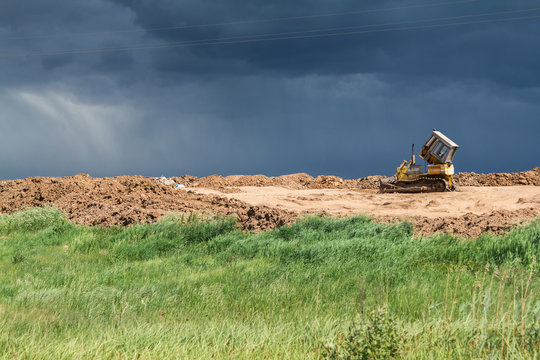 Old yellow lonely broken bulldozer in the field, against a stormy sky background