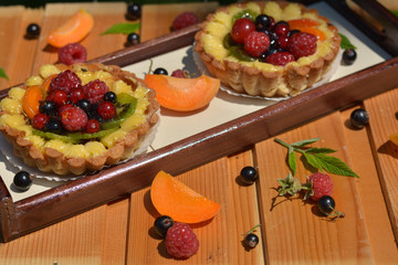 Fresh fruits tarts with raspberry, redcurrant, blackcurrant, peach, kiwi, cherry on wooden texture