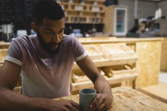 Thoughtful young man with coffee cup sitting at table