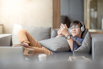 Young Asian man using smartphone taking a break relaxing on sofa during study in library, high school or university college student, educational concept