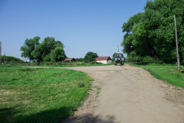 dirt road in the village. The path leads into the distance, where you can see the beautiful landscape, trees, lake and the sky. On a dirt road riding a tractor