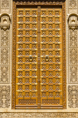 Fototapeta na wymiar Wooden door and ornament on wall of palace in Jaisalmer fort, India.
