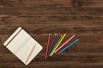Colored pencils and a notepad  on a wooden background. Copy space