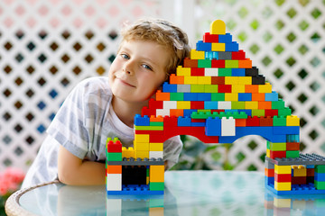 Little blond child and kid boy playing with lots of colorful plastic blocks.