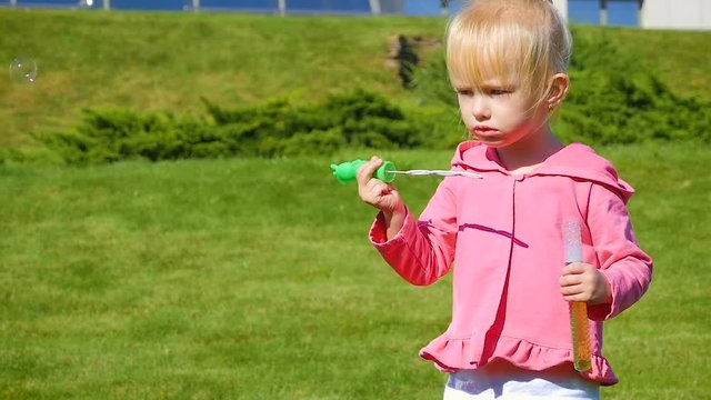 SLOW MOTION: little funny girl of three-years blowing soap-bubble in the city park.