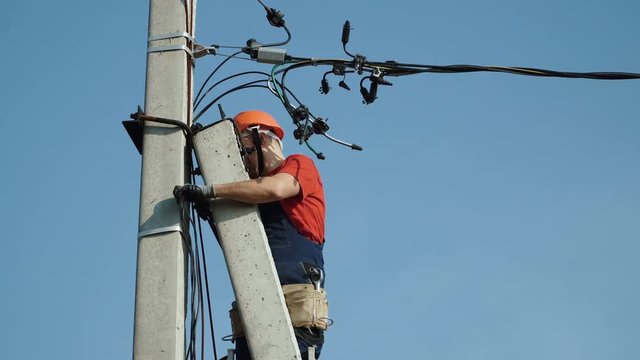 An electrician working at a newly installed utility pole - connects a new power line.