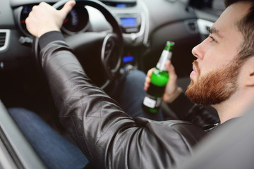Drunk young man with a beard with a bottle of beer in his hand behind the wheel of a car. Emergency...