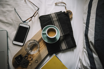 Delicious Morning fresh espresso coffee in Bed. Working at home essentials: Laptop, cup of coffee, smartphone, glasses, notebook on the hand-made wooden board in bed.