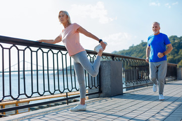 Senior woman doing stretching exercises while man jogging