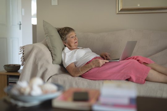 Senior woman lying on sofa using laptop in living room