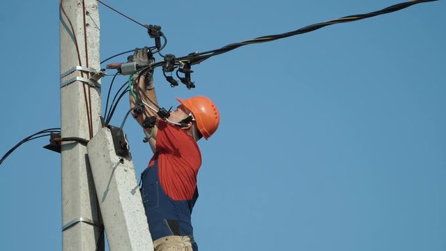An electrician working at a newly installed utility pole - connects a new power line.