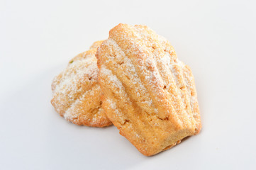 Freshly baked Madeleine cookies sprinkled with sugar powder 

close-up on the table, petite madeleine isolated on white 

background.