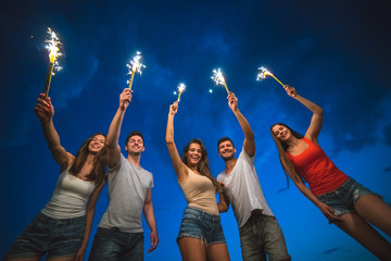 The happy people hold firework sticks. evening night time