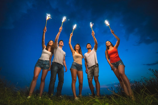 The happy people hold firework sticks. evening night time